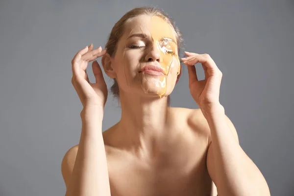 年轻的女人在她的脸上与灰色背景的蜂蜜 皮肤治疗 — 图库照片