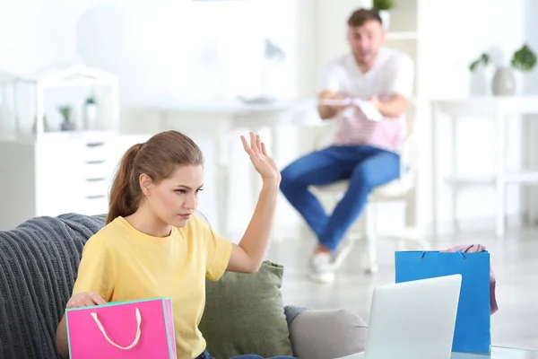 Mulher com sacos de compras e homem discutindo sobre dinheiro em casa. Problemas no relacionamento — Fotografia de Stock