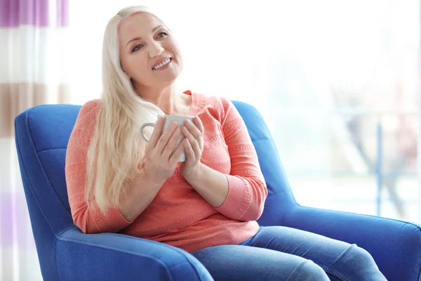 Mutlu olgun kadın evde koltukta otururken çay içme — Stok fotoğraf