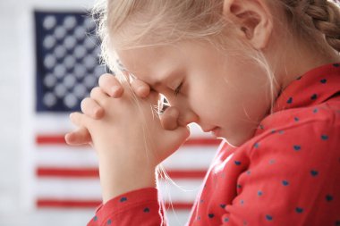 Cute little girl praying on American flag background clipart