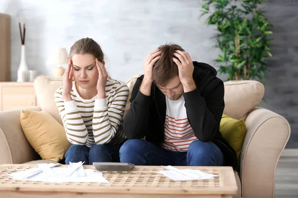 Pasangan muda yang tidak bahagia duduk di sofa dekat meja dengan tagihan. Masalah keuangan dalam hubungan — Stok Foto