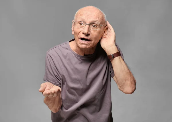 Homem idoso com problema auditivo em fundo cinza — Fotografia de Stock