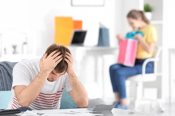 Upset man at table and woman with shopping bags in room. Money problems in relationship — Stock Photo, Image