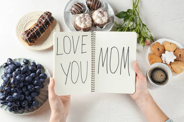 Kvinna som håller anteckningsboken med orden ”älskar dig mamma” vid bordet. Mors dag frukost — Stockfoto