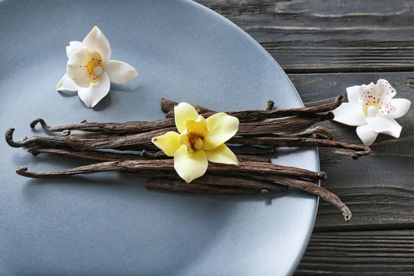 Piatto con bastoncini di vaniglia e fiori su sfondo di legno — Foto Stock