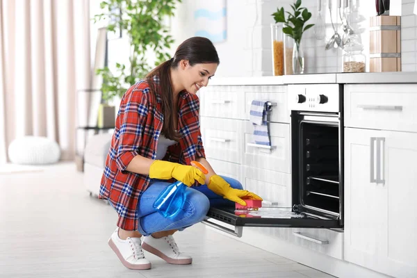 Young woman cleaning oven in kitchen — Stock Photo, Image