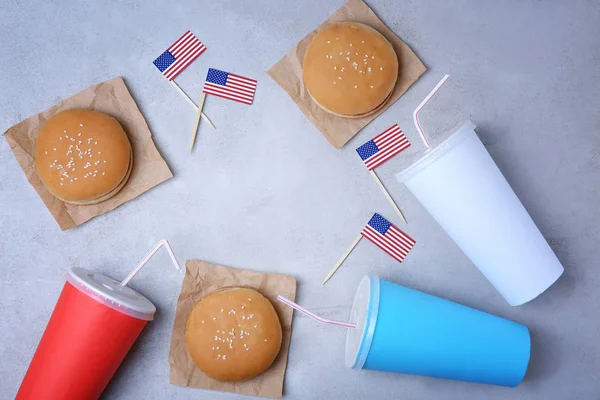 Sabrosas hamburguesas, tazas con bebidas y banderas americanas sobre fondo claro —  Fotos de Stock