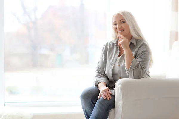 Porträtt av vacker mogen kvinna sitter i fåtölj hemma — Stockfoto