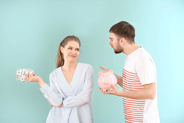 Счастливая женщина с деньгами и возмущенным мужчиной с копилкой на цветном фоне. Проблемы в отношениях
