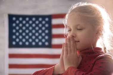 Cute little girl praying on American flag background clipart