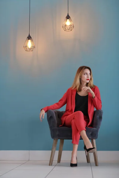 Красивая молодая стильная женщина сидит в кресле возле цветной стены — стоковое фото