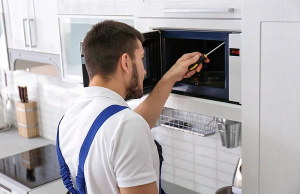 Jovem reparando forno de microondas na cozinha — Fotografia de Stock