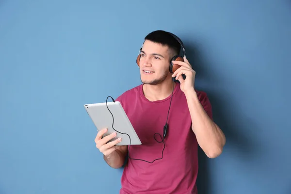 Homem ouvindo audiolivro através de fones de ouvido em fundo de cor — Fotografia de Stock