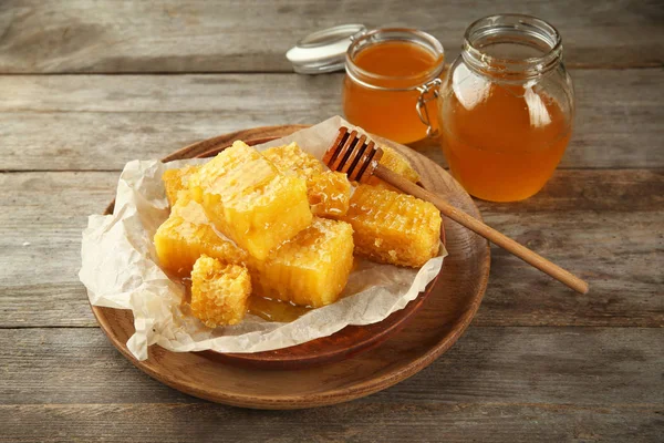 Frascos de mel doce e prato com pentes na mesa de madeira — Fotografia de Stock