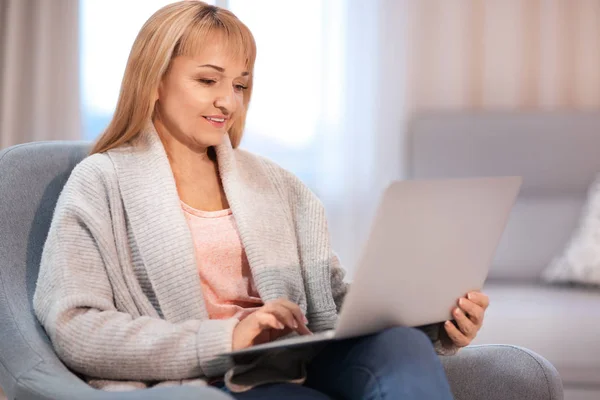 Glücklich reife Frau mit Laptop, während sie zu Hause im Sessel sitzt — Stockfoto