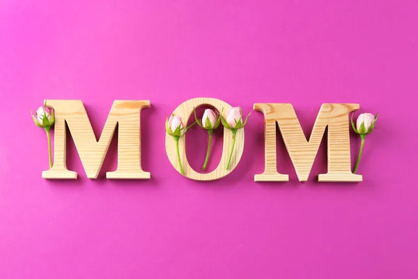 Palavra "mãe" e botões de rosa no fundo da cor. Celebração do dia da mãe — Fotografia de Stock