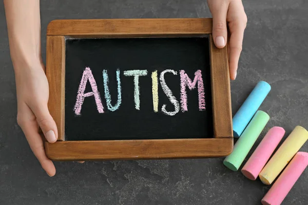 Mujer sosteniendo pizarra con palabra AUTISMO sobre fondo gris —  Fotos de Stock