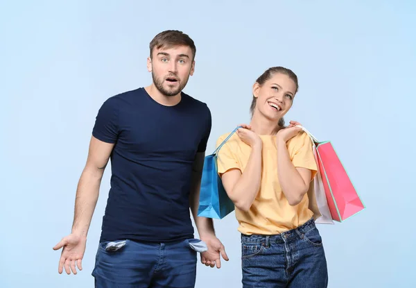 Mujer feliz con bolsas de compras y hombre indignado sobre fondo claro. Problemas de dinero en relación — Foto de Stock