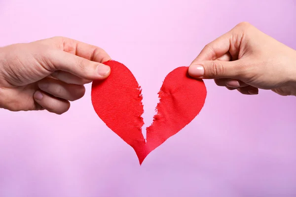 Pareja rasgando el corazón de papel por la mitad en el fondo de color, primer plano. Problemas de relación —  Fotos de Stock