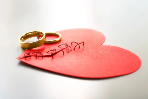 Paper heart cut in half and sewn back together with wedding rings on light background. Relationship problems — Stock Photo, Image