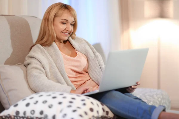 Glad mogen kvinna använder laptop medan du sitter i fåtölj hemma — Stockfoto