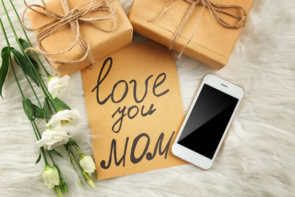 Caixas de presente, cartão com texto "Love you mom", smartphone e flores em fundo peludo. Celebração do dia da mãe — Fotografia de Stock