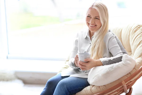 Счастливая зрелая женщина пьет чай, сидя в кресле дома — стоковое фото