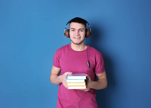 Man listening to audiobook through headphones on color background — Stock Photo, Image