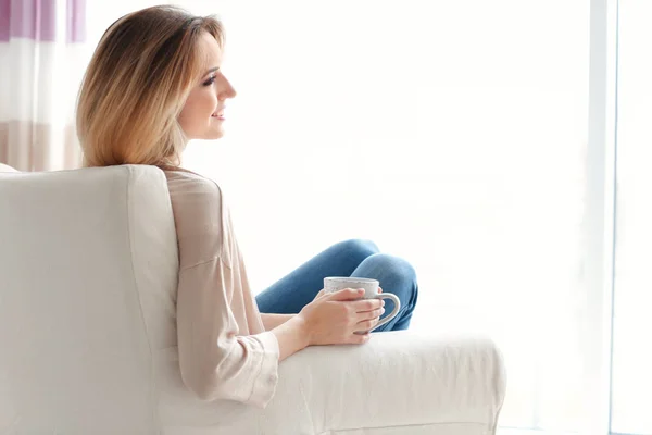 Jovem feliz bebendo chá enquanto se senta em poltrona em casa — Fotografia de Stock