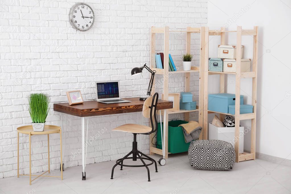 Comfortable home workplace with laptop on desk against brick wall