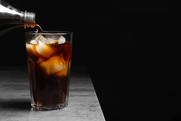 Despejando cola de garrafa em vidro com gelo na mesa contra fundo preto — Fotografia de Stock