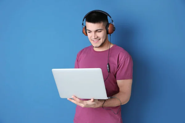Man listening to audiobook through headphones on color background — Stock Photo, Image