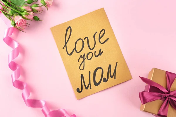 Carte avec texte "LOVE YOU MOM", fleurs et boîte cadeau sur fond de couleur. Salutations pour la fête des mères — Photo