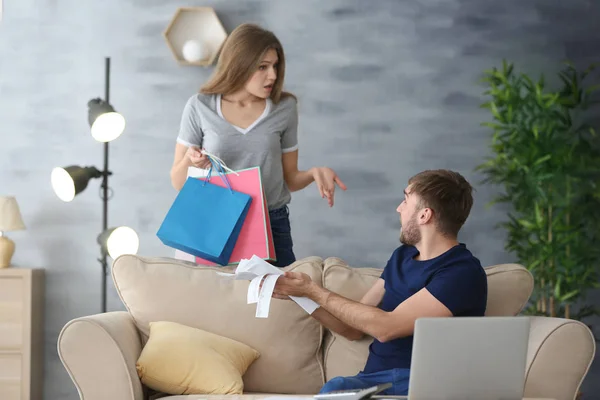 Mujer sosteniendo bolsas de compras y hombre con cuentas discutiendo por dinero en casa. Problemas en la relación — Foto de Stock
