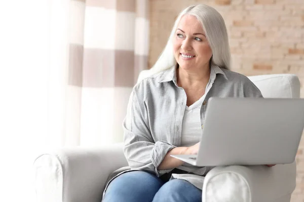 Szczęśliwy Starsza kobieta za pomocą laptopa siedząc w fotelu w domu — Zdjęcie stockowe