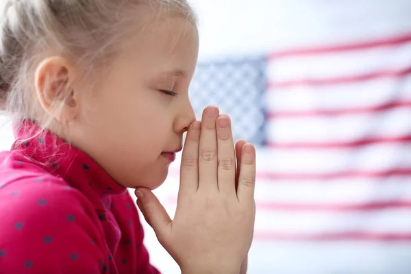 Niedliches kleines Mädchen betet auf amerikanischem Flaggenhintergrund — Stockfoto