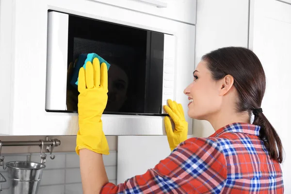 Jovem mulher limpeza forno de microondas na cozinha — Fotografia de Stock