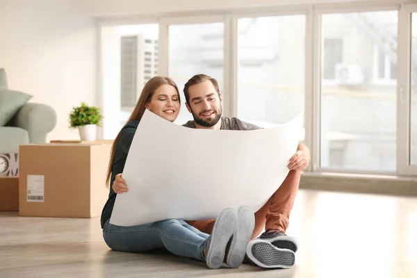 Casal jovem com plano de casa sentado no chão depois de se mudar para uma nova casa — Fotografia de Stock