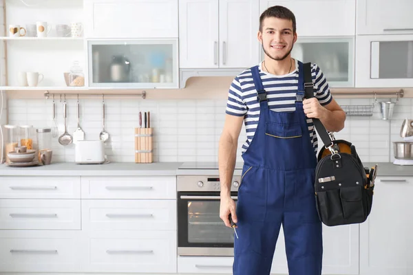 Trabajador joven con bolsa de herramientas de pie cerca del horno en la cocina —  Fotos de Stock