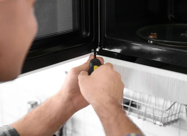 Young man repairing microwave oven, closeup