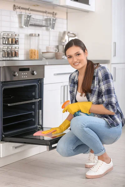 Young woman cleaning oven in kitchen — Stock Photo, Image