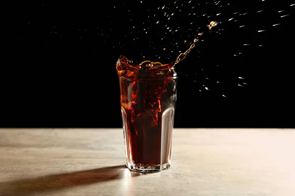 黒の背景にテーブル上にガラスにコーラのスプラッシュ — ストック写真