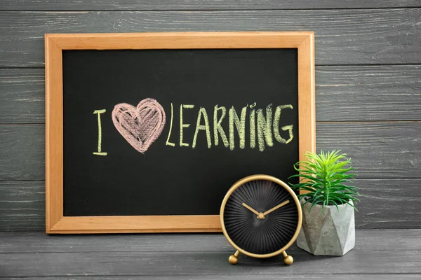 Pizarra con frase "Me encanta aprender" y despertador en la mesa. Tiempo para estudiar — Foto de Stock