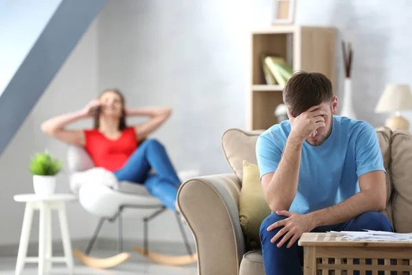 Sad man vid bord med räkningar och suddig kvinna på bakgrunden. Pengar problem i relation — Stockfoto