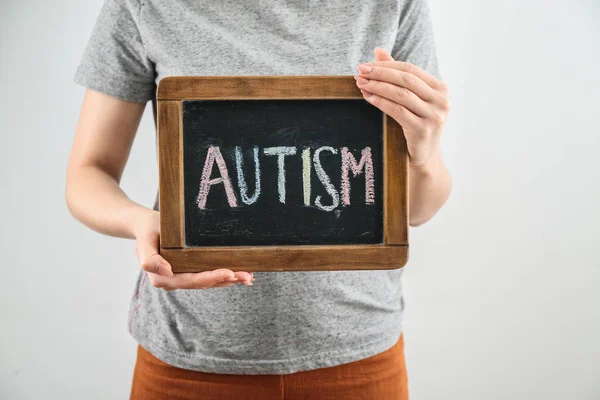 Mujer sosteniendo pizarra con palabra AUTISMO sobre fondo claro — Foto de Stock