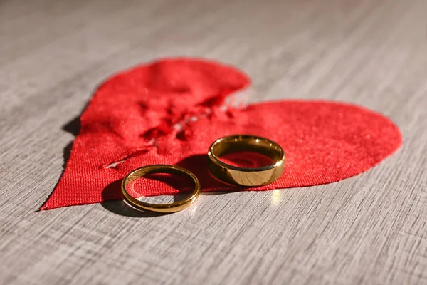 Corazón de tela rota y anillos de boda sobre fondo de madera. Problemas de relación — Foto de Stock