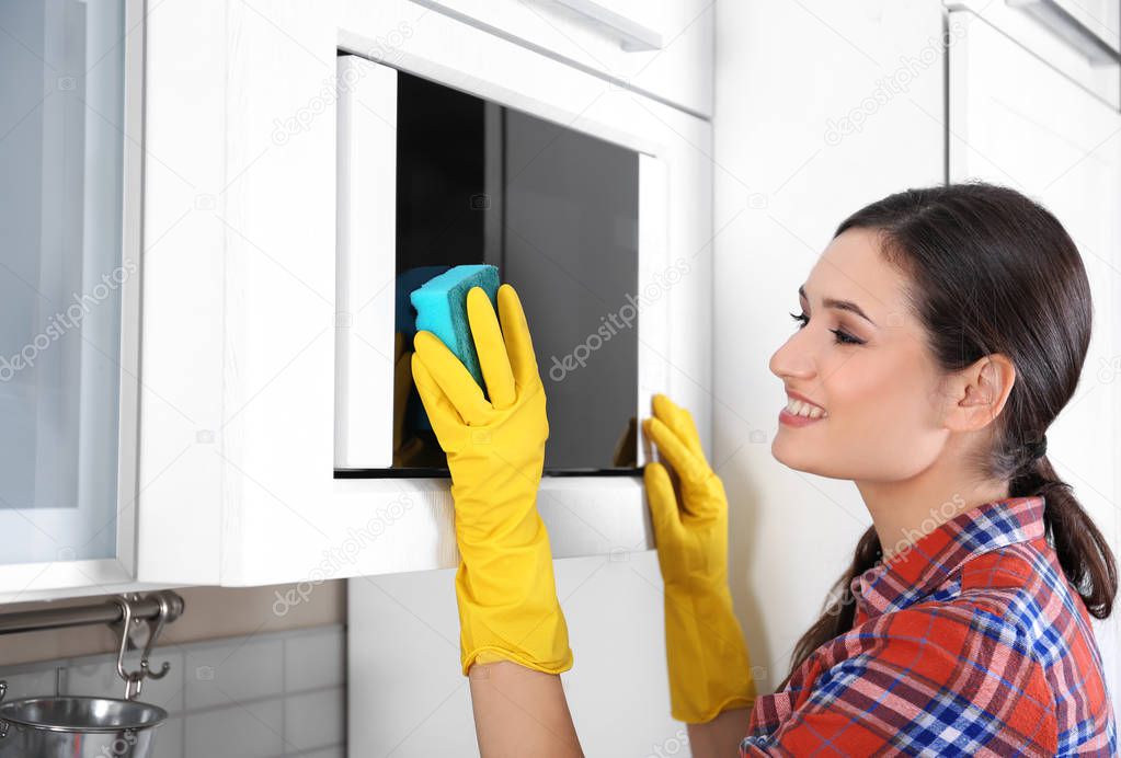 Young woman cleaning microwave oven in kitchen