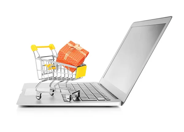 Laptop en kleine winkelwagentje met de doos van de gift op witte achtergrond. Internet shopping concept — Stockfoto
