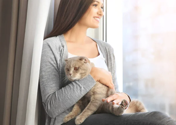 Jovem mulher com gato de estimação bonito sentado no peitoril da janela em casa — Fotografia de Stock