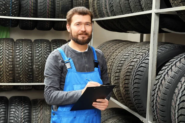 Venditore con appunti vicino pneumatici in negozio di automobili — Foto Stock